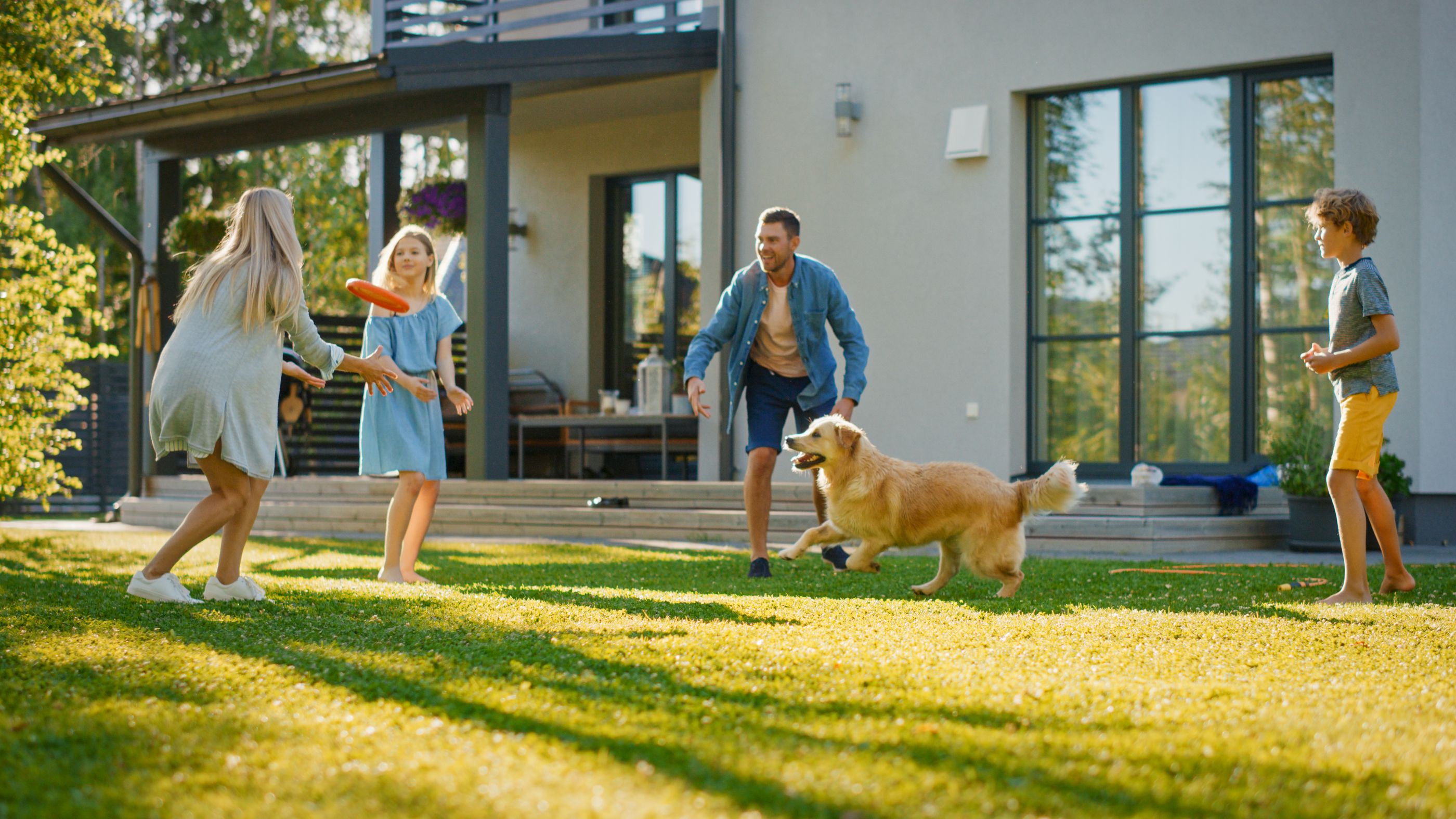 A family and a golden retriever playing on an artificial turf lawn behind a modern house